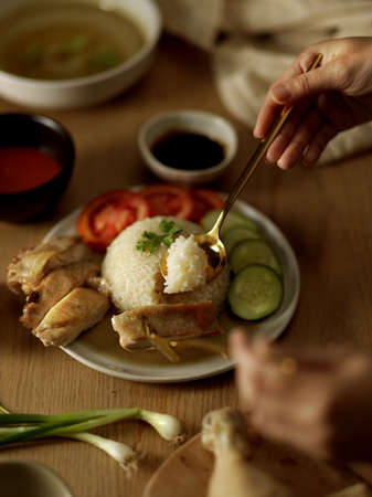 Cropped shot of woman eating Hainanese chicken rice (steamed chicken rice) with spoon and forkの写真素材
