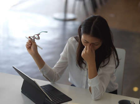 Portrait of female office worker feeling tired while working in office roomの写真素材