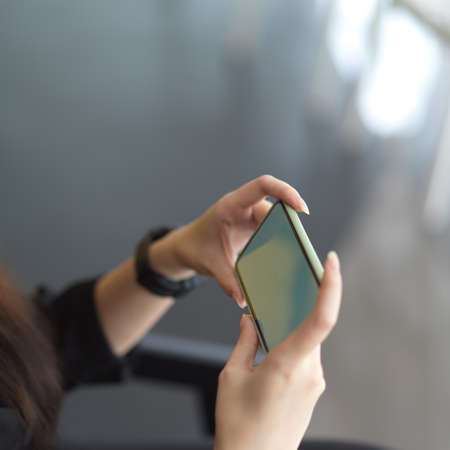 Cropped shot of female hands holding horizontal smartphone in blurred backgroundの写真素材