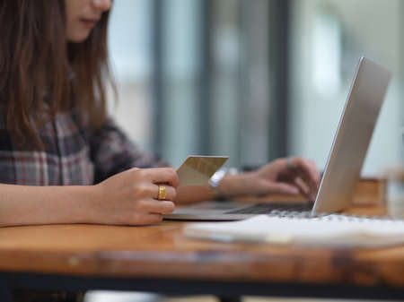 Side view of female student holding credit card while online payment on laptop in home office roomの写真素材