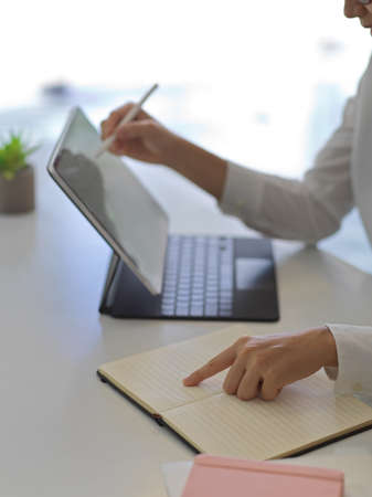 Side view of female hands working with digital tablet and notebook on white table