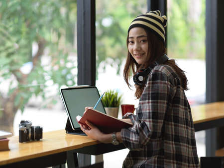 Portrait of female teenager doing assignment with digital tablet and textbook in cafeの写真素材