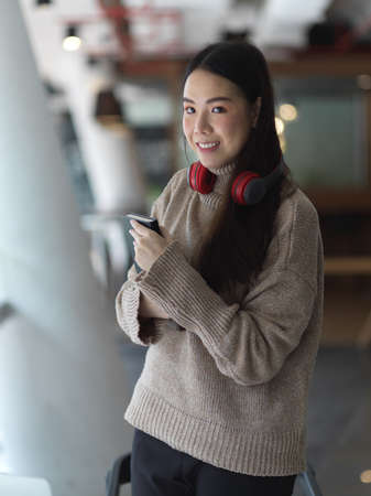 Portrait of female in sweater with headphone holding book while standing in office