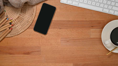 Top view of wooden table with smartphone, coffee cup, keyboard, pencils and copy spaceの写真素材