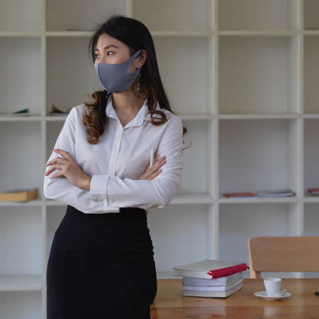 Portrait of female office worker wearing mask while standing in office roomの写真素材