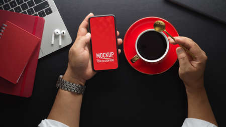 Overhead shot of male hand holding smartphone while take a coffee break on workspace