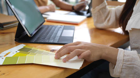 Side view of female designer working with tablet and colour swatch on wooden tableの写真素材
