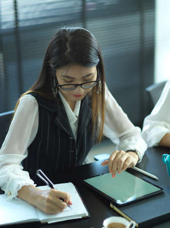 Portrait of female office worker taking note while meeting with her team in meeting room