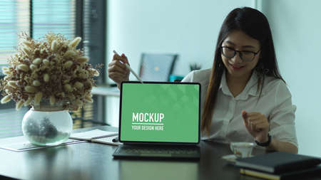 Portrait of female office worker showing laptop screen include clipping path on office deskの写真素材