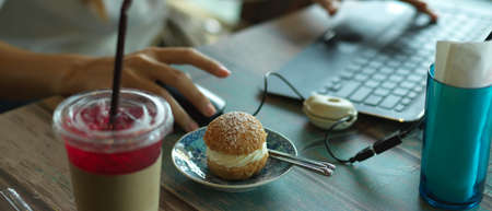 Cropped shot of workspace with beverage, snack and female using laptop in cafe