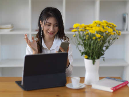 Young beautiful businesswoman using her smartphone while working with tablet