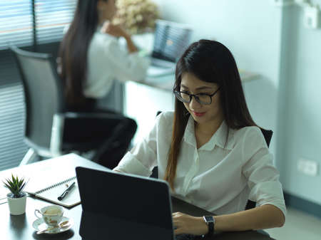 Cropped shot of young female office worker working with tablet with her coworker in the backgroundの写真素材