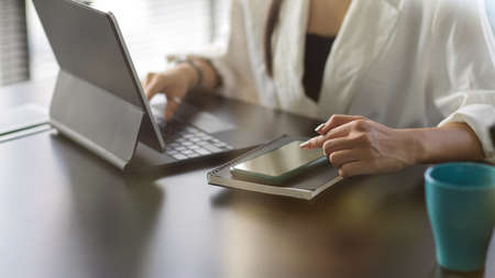 Cropped shot of young businesswoman working on her project with tablet while using smartphone