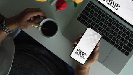 Top view of man holding mock up blank screen smartphone while holding coffee cup on working table, clipping pathの写真素材