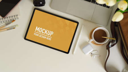 Top view of workspace with tablet, laptop, accessories and supplies on white table