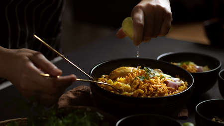 Close up view of hand squeezing lime juice onto Noodles curry soup with Chicken (Khao Soi), Northern Thai foodの写真素材