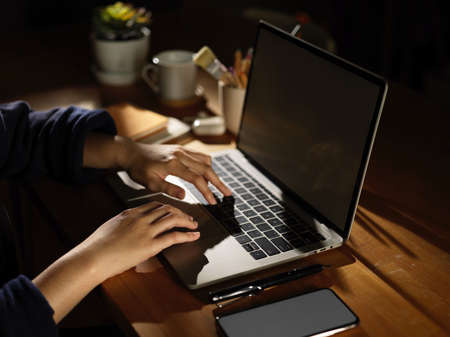 Side view of female hand typing on laptop on wooden table with smartphone and suppliesの写真素材