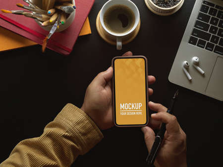 Top view of male hands using smartphone on workspace with supplies