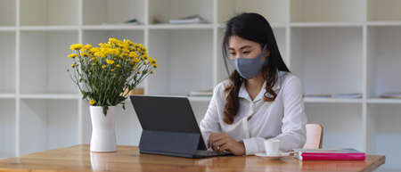 Portrait of female wearing mask and working with digital tablet on wooden table
