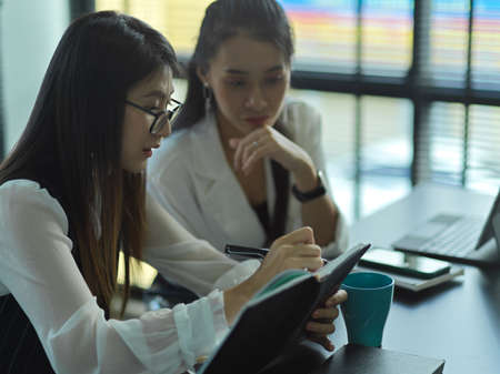 Side view of two young female businesspeople consulting on their project in meeting roomの写真素材
