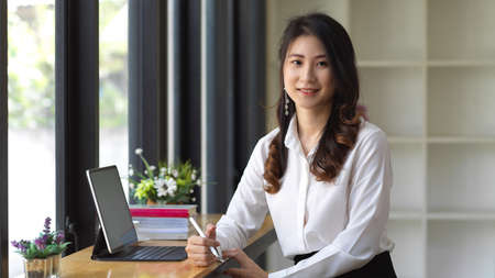 Portrait of female student looking into camera while doing assignment with digital tablet in cafeの写真素材