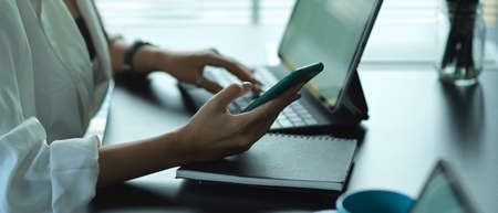 Side view of female hand working with smartphone and digital tablet on office tableの写真素材
