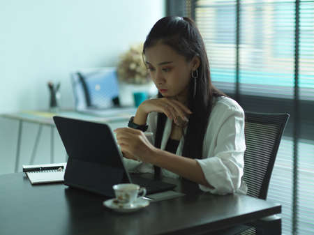 Young professional businesswoman focusing on her project while working with tablet in modern office roomの写真素材