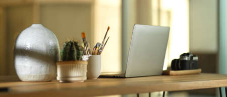 Cropped shot of workspace with laptop, camera, paint brushes and decorations in office roomの写真素材
