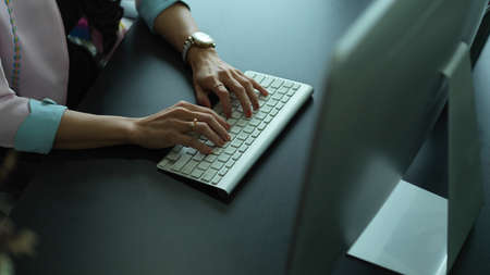 Cropped shot of female hands typing on wireless computer keyboard on office deskの写真素材