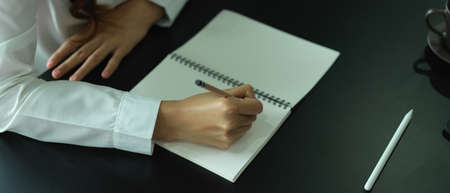 Side view of female office worker writing on blank notebook on office tableの写真素材