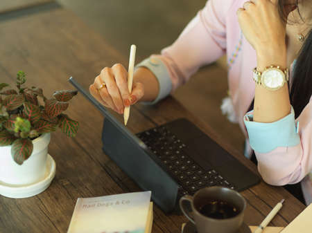 Cropped shot of female freelancer working with digital tablet on wooden table in cafe