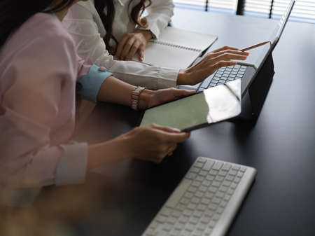 Side view of two female workers working together on their project with digital devices in meeting roomの写真素材