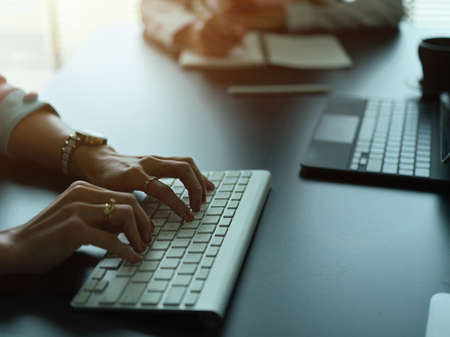 Side view of female hands typing on wireless computer keyboard on office deskの写真素材