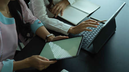 Side view of two female workers working together on their project with digital devices on meeting...