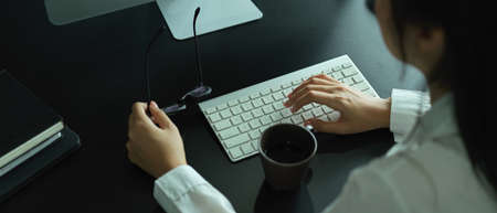 Overhead shot of female hand holding eyeglasses and typing on computer keyboard on office deskの写真素材