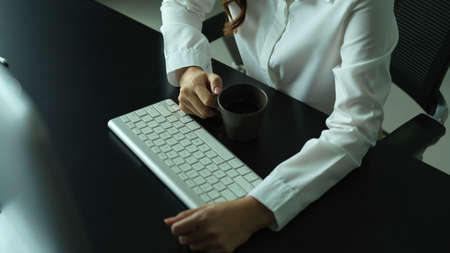Close up view of female hand holding coffee mug on office desk with computer keyboardの写真素材