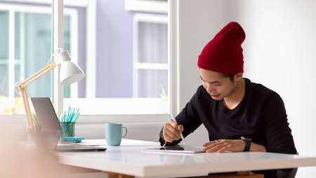 Portrait of young man working with digital tablet on white table in home office roomの写真素材