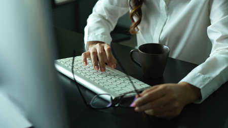 Cropped shot of female hand holding eyeglasses and typing on computer keyboard on office deskの写真素材