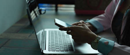 Side view of female hands using mock up smartphone while working with laptop on plank tableの写真素材