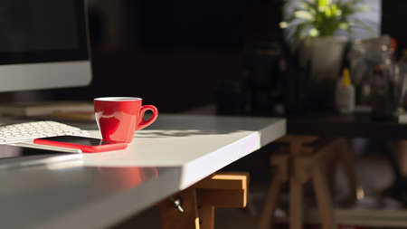 Cropped shot of red coffee cup on computer table with smartphone and supplies in home office roomの写真素材