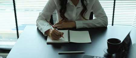 Close up view of female office worker writing on blank notebook on meeting tableの写真素材