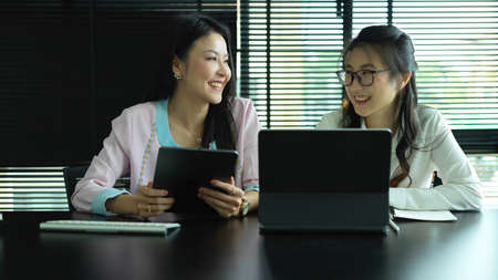 Portrait of two businesswomen consulting on their project with digital devices in meeting roomの写真素材