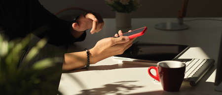 Side view of hands using smartphone on white table with coffee cup and suppliesの写真素材