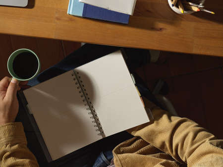 Top view of male office worker reading schedule book while holding coffee cup at workplace