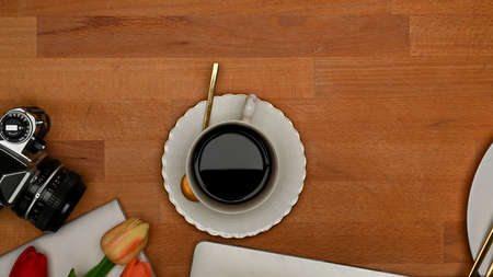 Top view of wooden table with coffee cup, camera, supplies, copy space and flower decorated on the tableの写真素材
