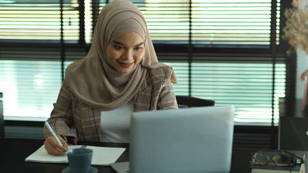 Portrait of Asian muslim businesswoman working with laptop and supplies in office room