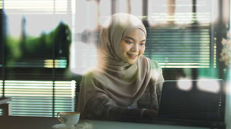 View through glass wall of young muslim businesswoman working with digital tablet in office roomの写真素材