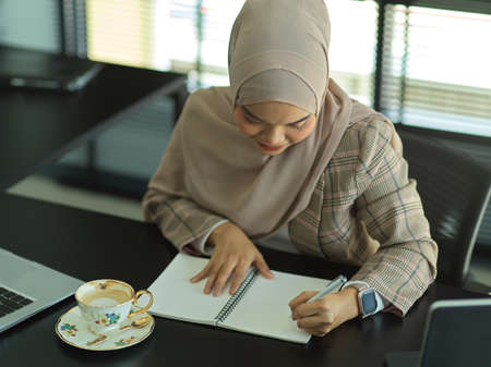 Portrait of Asian muslim businesswoman writing on notebook while working in office roomの写真素材