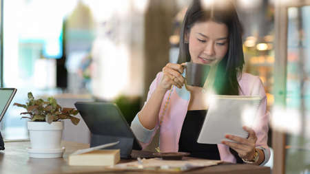 View through glass wall of businesswoman taking coffee break and looking on schedule book