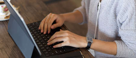 Side view of female hands typing on tablet keyboard on wooden table